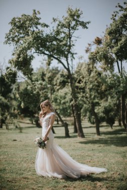 Beyaz modern bir hippi elbisesi içinde yürüyen bir gelin portresi. Günbatımında ormanda eski moda elbiseli beyaz sarışın gelin. Bir buket çiçekle poz veren çekici bir bayan.