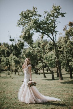 Beyaz modern bir hippi elbisesi içinde yürüyen bir gelin portresi. Günbatımında ormanda eski moda elbiseli beyaz sarışın gelin. Bir buket çiçekle poz veren çekici bir bayan.