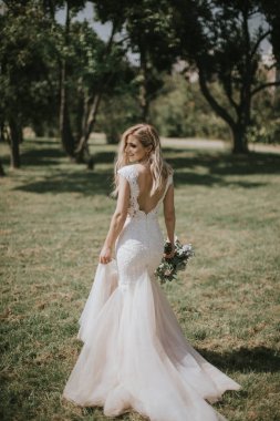 Beyaz modern bir hippi elbisesi içinde yürüyen bir gelin portresi. Günbatımında ormanda eski moda elbiseli beyaz sarışın gelin. Bir buket çiçekle poz veren çekici bir bayan.