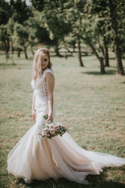 Beyaz modern bir hippi elbisesi içinde yürüyen bir gelin portresi. Günbatımında ormanda eski moda elbiseli beyaz sarışın gelin. Bir buket çiçekle poz veren çekici bir bayan.