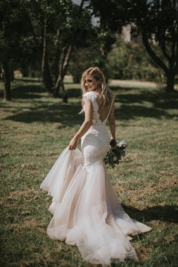 Beyaz modern bir hippi elbisesi içinde yürüyen bir gelin portresi. Günbatımında ormanda eski moda elbiseli beyaz sarışın gelin. Bir buket çiçekle poz veren çekici bir bayan.