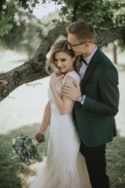 Güzel bir gelin ve damadın portresi kucaklaşır, öpüşür ve kucaklaşır. Doğanın bağrında aşık bir çift. Yakışıklı damat ve ormanda poz veren güzel sarışın gelin. Modern elbise ve takım elbise