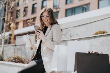 Alışveriş torbaları ve akıllı telefonları olan çekici bir kız. Arka planda modern şehir megapolis 'i var. İnternetten sipariş veren ve alışveriş yapan bir bayan. Güzel beyaz kadın.