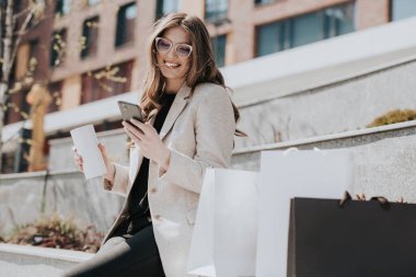 Alışveriş torbaları ve akıllı telefonları olan çekici bir kız. Arka planda modern şehir megapolis 'i var. İnternetten sipariş veren ve alışveriş yapan bir bayan. Güzel beyaz kadın.