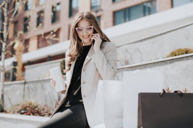 Alışveriş torbaları ve akıllı telefonları olan çekici bir kız. Arka planda modern şehir megapolis 'i var. İnternetten sipariş veren ve alışveriş yapan bir bayan. Güzel beyaz kadın.