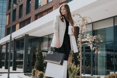 Alışveriş torbaları ve elinde sıcak içeceklerle çekici bir kız. Arka planda modern şehir megapolis 'i var. İnternetten sipariş ve alışveriş. Güzel beyaz kadın.