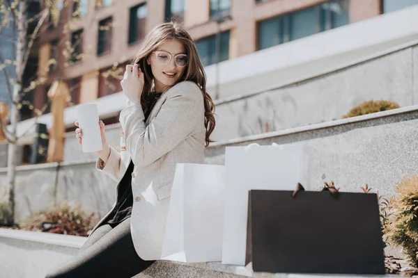 ショッピングバッグと温かい飲み物を手にした魅力的なかわいい女の子 近代都市の大都市を背景に 女性の注文とオンラインショップ 美しい白人女性 ストック写真