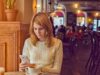 Kadın beyaz cep telefonu ekranına bakarak kafede. Kahve fincan