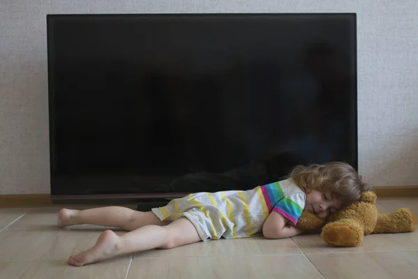 Retrato conceitual menina está dormindo no chão no fundo de uma tela de TV preta — Fotografia de Stock