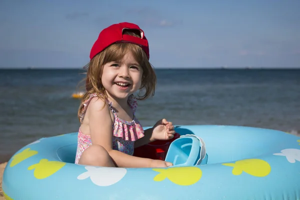 Linda niña en una gorra roja jugando en la playa contra el mar azul — Foto de Stock