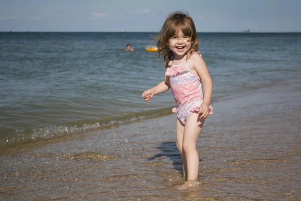 Niño pequeño en un traje de baño está de pie junto al mar y sonriendo — Foto de Stock