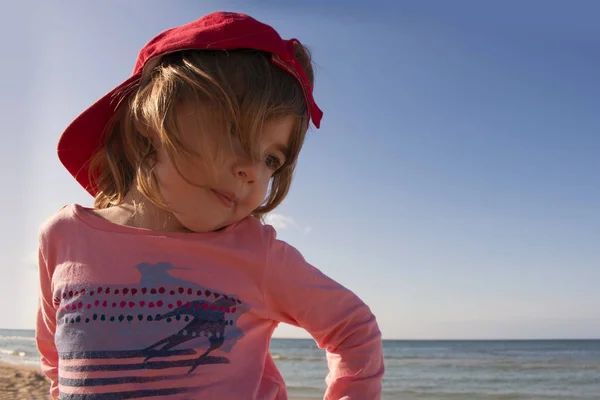 Retrato de cerca de un niño pequeño lindo y sonriente en la playa con una gorra roja — Foto de Stock