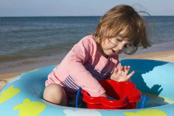 Niña linda se sienta en una piscina para niños en el fondo de la playa del mar — Foto de Stock