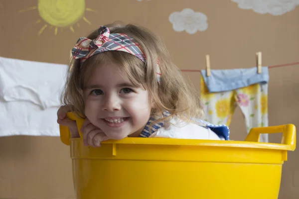 Cute little girl smiles and sits in a yellow bath — Stock Photo, Image