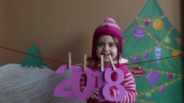 Concetto di Capodanno 2018. Bella bambina che decora il numero di Capodanno. sfondo di un albero di Natale dipinto e neve — Video Stock