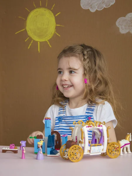 Linda niña divertida preescolar jugando con bloques de juguete de construcción construyendo una torre en la sala de jardín de infantes. fondo pintado por el sol y las nubes — Foto de Stock