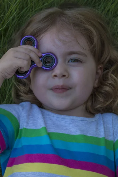 Pequeña chica hermosa está jugando spinner azul en la mano . — Foto de Stock