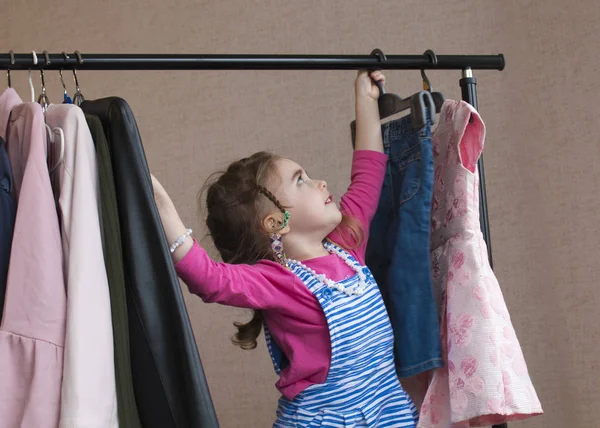 Adorable niña eligiendo ropa en perchero — Foto de Stock
