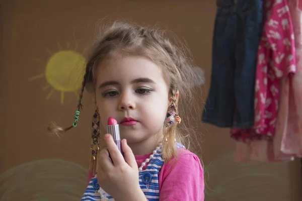 Güzel küçük kız rahat kıyafetler içinde bir lipstic tutuyor. arka plan boyalı güneş