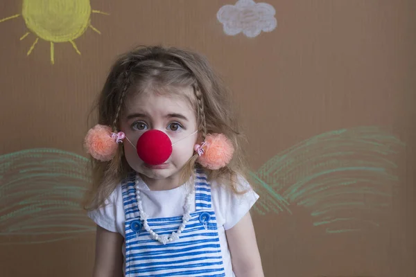 Portret figlarny dziewczynka sobie nos klauna i warkocze na tle domu malowane słońcem i białe chmury — Zdjęcie stockowe