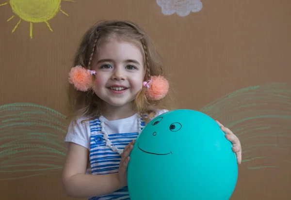 Mutlu kız ve yeşil balon tutan pigtails portresi. Arka plan beyaz bulutlar ve boyalı güneş