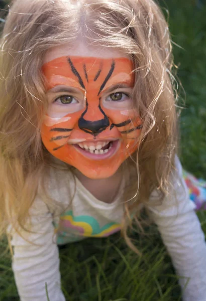 Retrato emocional de cerca de una niña con maquillaje de tigre aqua, sonriendo y sentada en un parque . — Foto de Stock