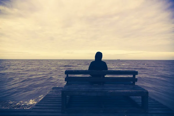 Il giovane si siede su una sedia di legno nel mare Foto Stock