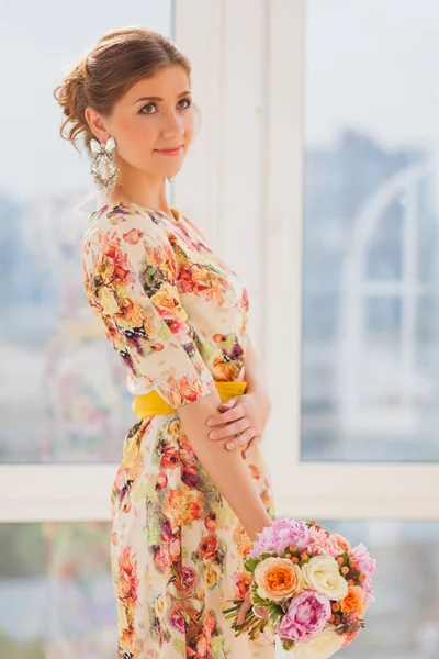 Hermosa chica en un vestido largo de pie cerca de una ventana con un ramo —  Fotos de Stock