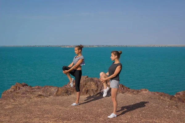 2 人の女の子は、ビーチでヨガの瞑想を行っています。スポーツと健康的なライフ スタイルのコンセプトです。夏の休日 — ストック写真