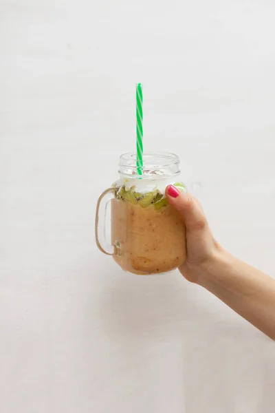 Meyve yüzlü - sağlıklı beslenme kavramı. Muz, kivi ve mason kavanoza yoğurt ile smoothies close-up. Kız bir cam kavanoz onun elinde tutuyor
