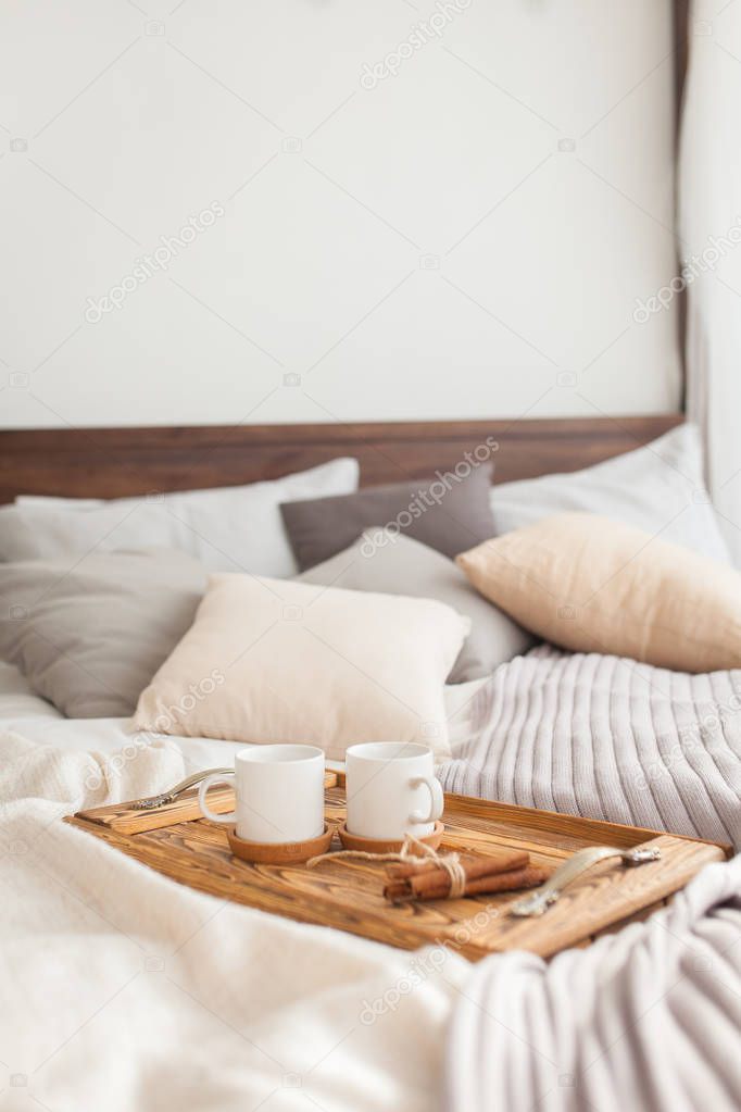 Two mugs on a tray white bed with a cinnamon stick, breakfast concept