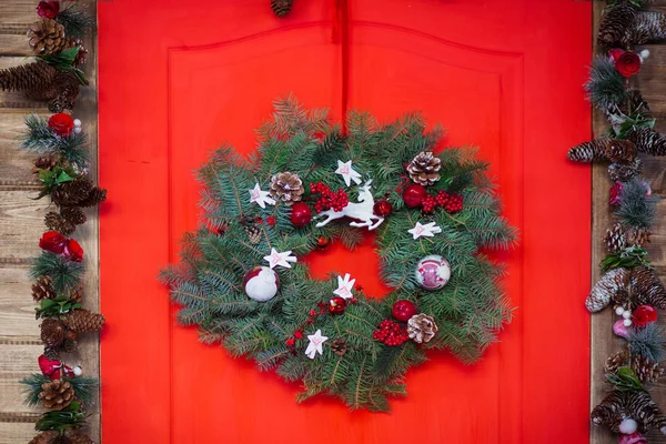 Christmas wreath made of spruce branches, red balls, cones on the wooden background