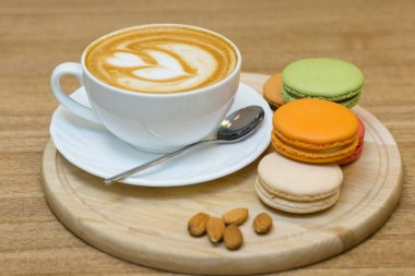 Cup of cappuccino coffee with macaroons and nuts on wooden table