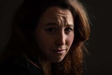 Siyah arka planda kameraya bakan üzgün esmer kızın sade portresi. Kadın yüzünde duygular.