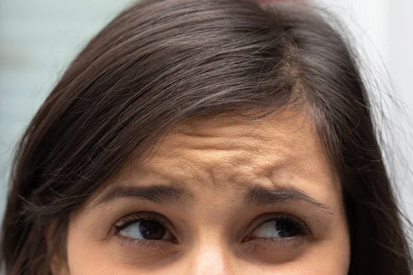 A closeup view on the eyes and forehead a thirty something Caucasian lady frowning with brunette hair.