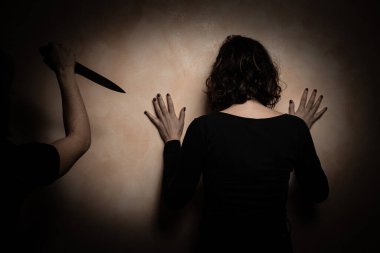 Esmer bir kadının dikiz aynasından bej bir duvara yaslanışı. Keskin bıçaklı bir adam aile içi şiddet mağduruna saldırıyor. Kadınlara karşı şiddet kavramı