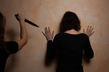 Bej duvarın yanında duran depresif kadının dikiz görüntüsü. Keskin bıçaklı bir adam aile içi şiddet mağduruna saldırıyor. Kadınlara karşı şiddet kavramı