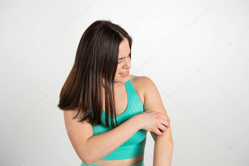 Nice brown haired girl scratching her arm, it itches her. Emotional expression of female athlete model isolated over white background. Active and healthy lifestyle, emotions concept