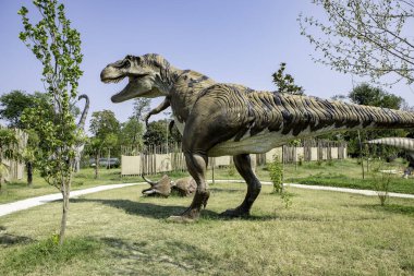 Pençeleri açık ve tehditkar bakışları olan T-rex parkta yürüyor