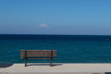 Yaz boyunca kıyı şeridindeki boş bir bankın manzarası, açık mavi gökyüzü, sakin okyanus ve kopyalanacak yer.