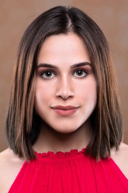 Kahverengi omuz hizasında saçları olan güzel bir kızın yüzüne yakından bakmak. Kameraya doğru bakıyor koyu renk göz farı ve kırmızı dudaklı göz kalemi kullanıyor..