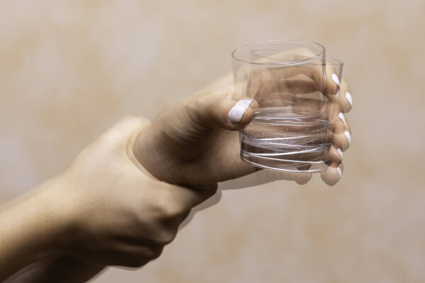 A closeup view on the hands of a person trying to hold a glass of water steady, shaking hands symptomatic of a central nervous and motor system disease such as Parkinson's