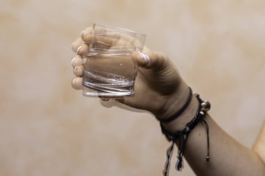 A closeup view on the hands of a girl trying to hold a glass of water still, tremors due to Parkinson's disease making drinking and eating difficult for people with the disease. clipart