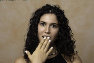 20 yaşında güzel bir kız çocuğu, beyaz lavantalı tırnakları ve dalgalı esmer saçlarıyla elini açık tutup tarafsız bir arkaplanda dururken şok içinde nefes nefese kalırken görülüyor..