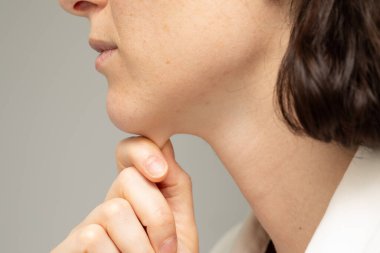 30 'lu yaşlarda ince yapılı beyaz bir kızın, çenesinin altındaki ince yağ tabakasını sıkarken yakın çekim ve yan profil görüntüsü. Vücut bozuklukları ve yaşam tarzı kavramları.