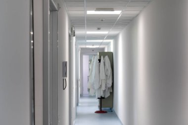 Beyaz bilim ceketleri steril bir odanın yakınında bir ilaç araştırma laboratuarının içinde asılı olarak görülüyor. Bilim adamları çalışma alanına girmeye hazır..
