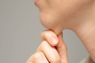 A close-up and side profile view of a young Caucasian woman pinching the layer of fat under her chin with her fingers. Commonly called a double chin, worries about her appearance. clipart