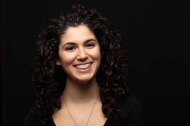 Gülümseyen siyah saçlı, kahverengi gözlü, başı eğik bir kızın yakın çekimi.