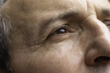 Yaşlı bir erkeğin kahverengi gözüne yakından ve detaylı bir bakış açısı. Düşüncelere dalmış yaşlı bir adamın göz ve alnında kırışıklıklar ve kırışıklıklar görülür..