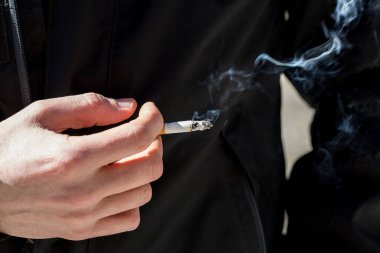 Kafkasyalı birinin elinde sigara içen birinin yakın çekim görüntüsü. Kötü sağlık ve kanserojen kavram.